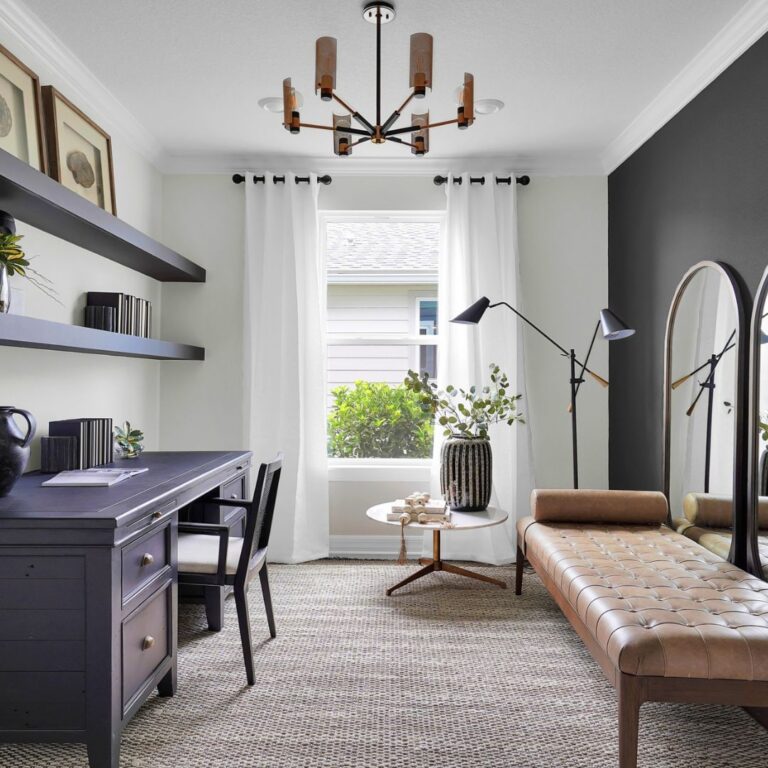 Modern home office with a black desk, shelves, leather daybed, floor mirror, round side table, and large window with white curtains letting in natural light.