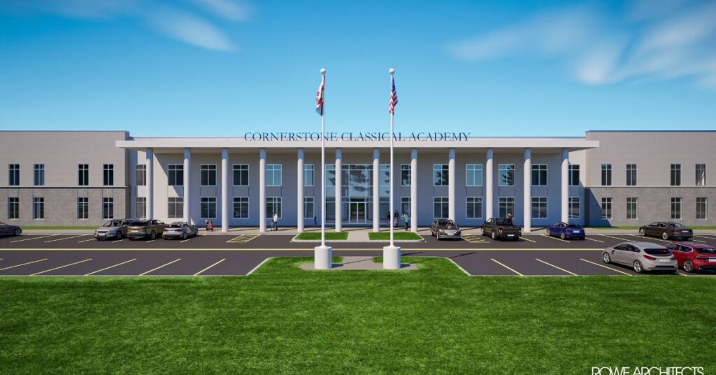 A two-story school building with columns, labeled "Cornerstone Classical Academy," has cars parked in front and three flagpoles on a clear day.
