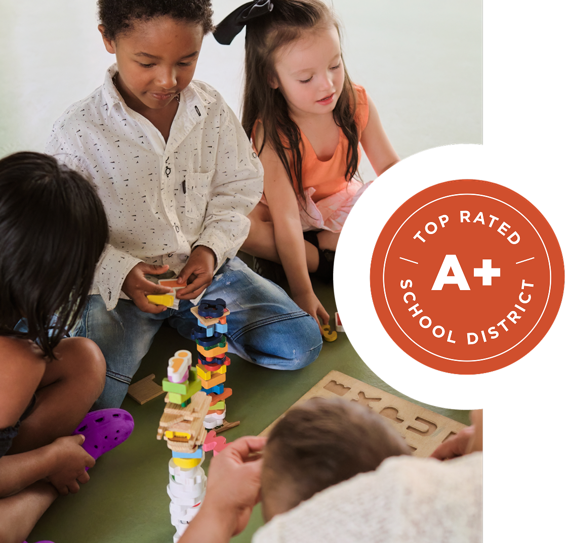 Four young children play with colorful stacking blocks and puzzles on the floor. A circular badge reads "Top Rated School District A+.
